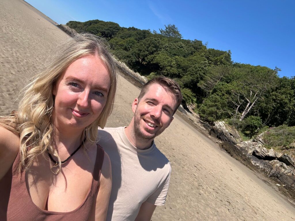 Author and partner on the beach at port meirion , beautiful view behind them